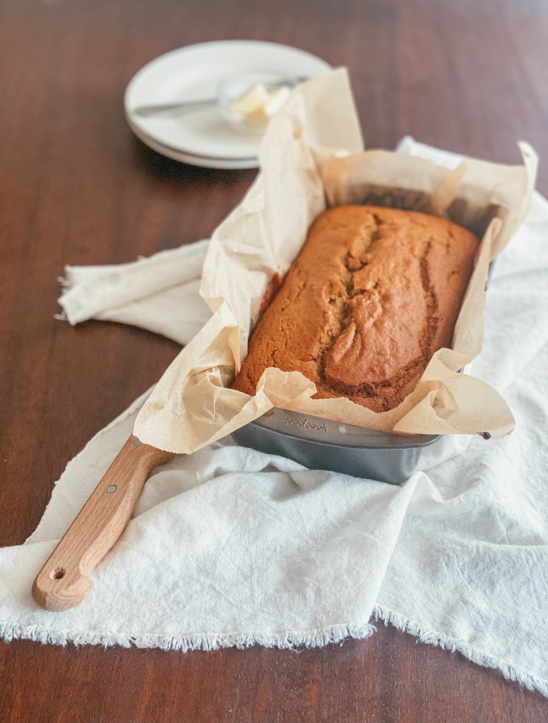 pumpkin bread loaf in a loaf pan with parchment paper sitting on a white cloth with a knife