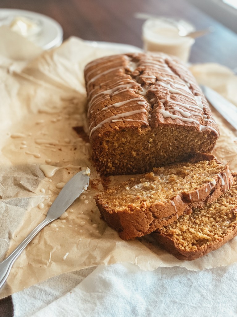 pumpkin bread with maple glaze over parchment paper and white cloth with glaze and butter in the background