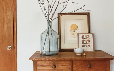 wood dresser with vase of branches and two watercolor fruit and nut prints and a candle in front